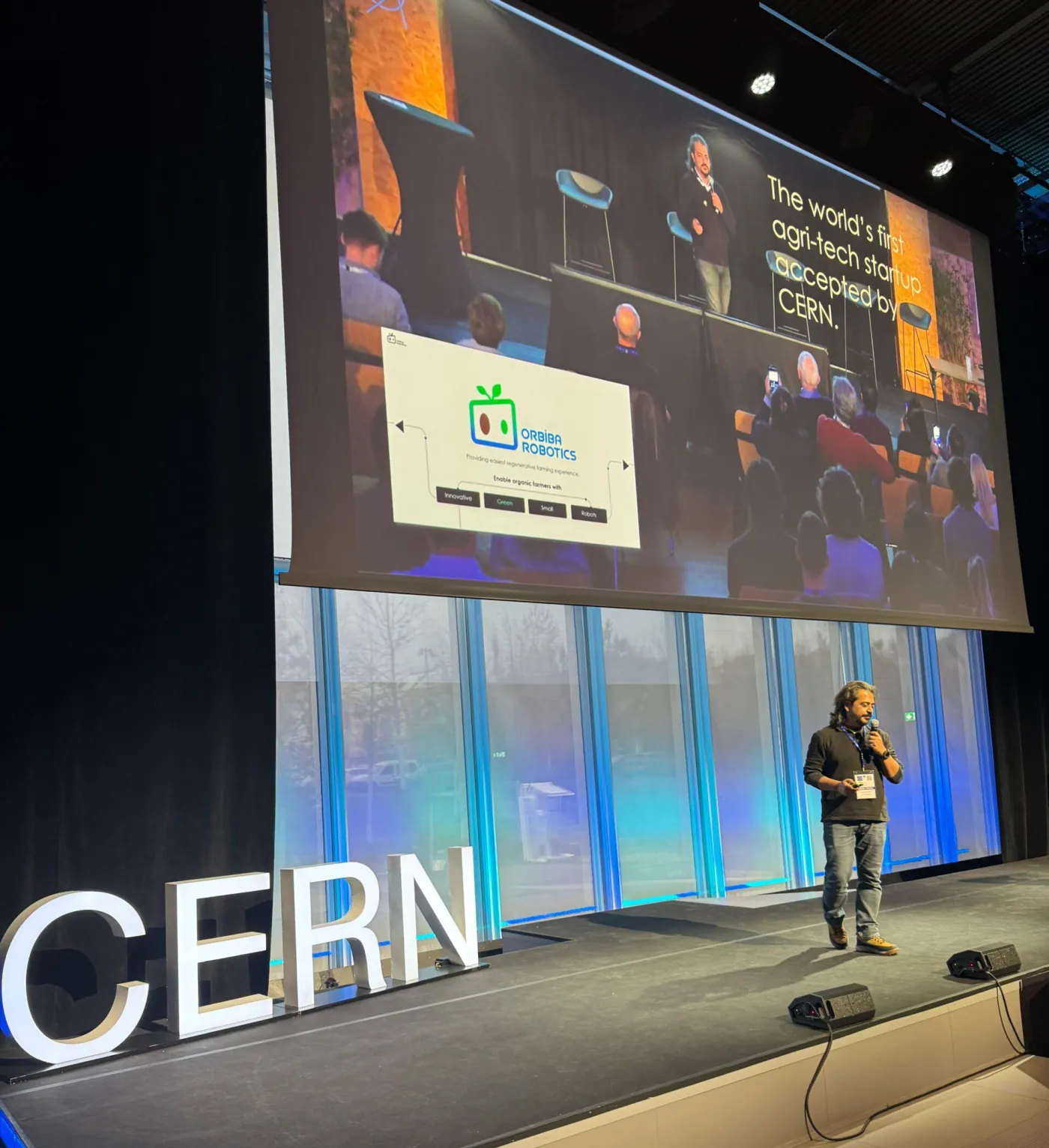Ilker Bektas presenting on stage at CERN with an Orbiba Robotics slide behind him